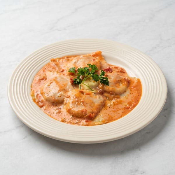 Ravioli pasta in a creamy tomato sauce, garnished with fresh parsley on a white plate.
