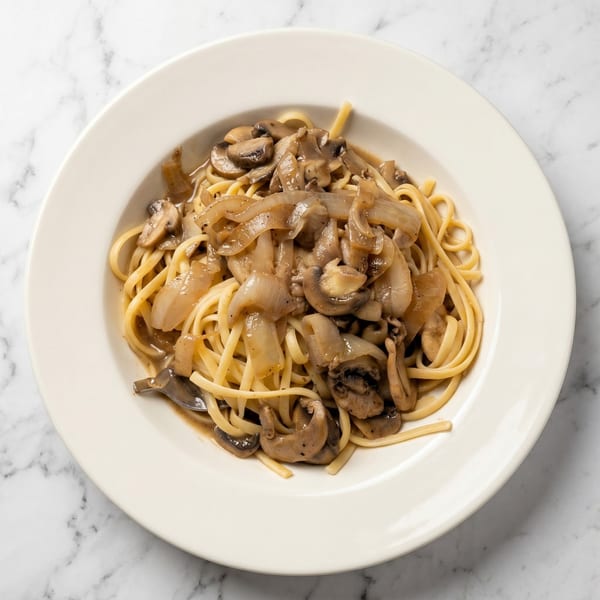 Linguine pasta with sautéed mushrooms and onions in a light sauce, served in a white bowl.