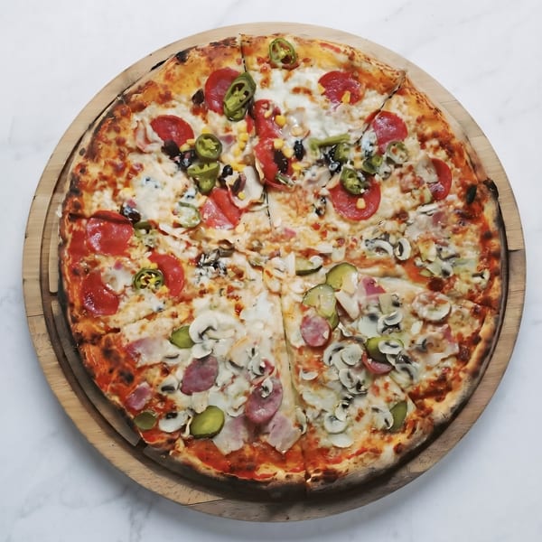 A large, round pizza with various toppings, including pepperoni, mushrooms, and jalapeños, on a wooden board.
